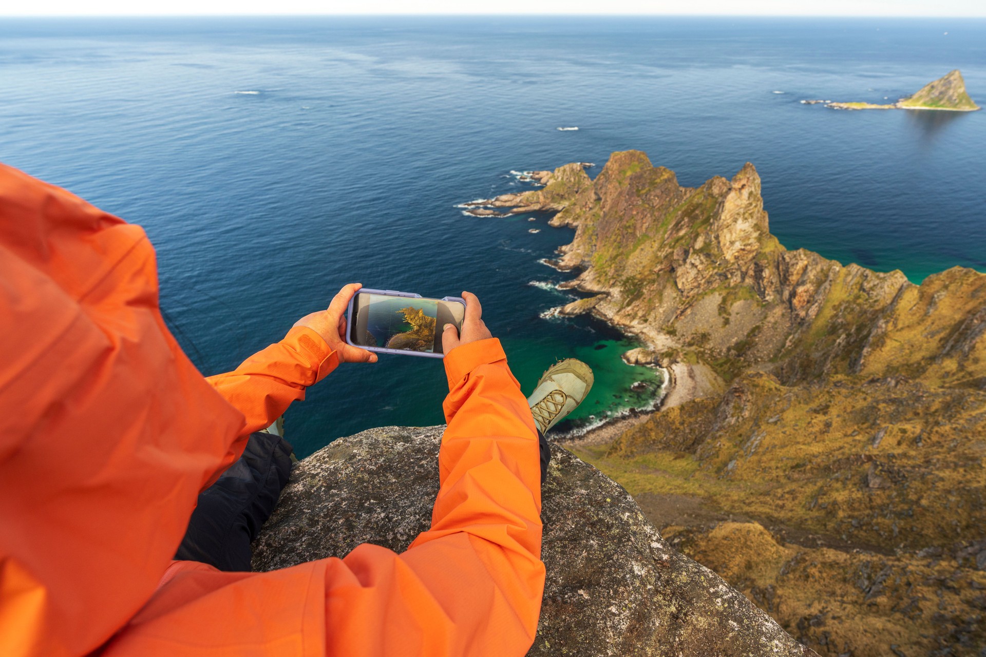 Hiker photographing mountains above the ocean, Norway